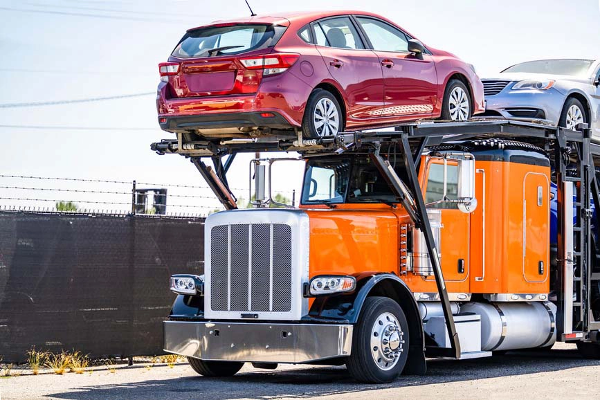 A loaded black and orange open auto transport truck.