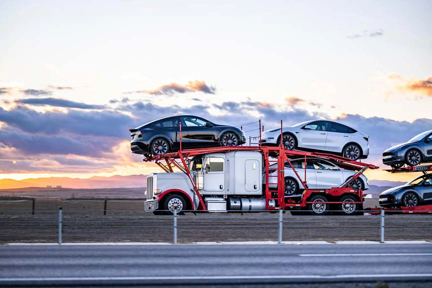 A fully loaded auto transport semi driving on a desert highway during sunset.